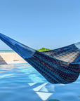 Blue hammock by a pool with palm trees and clear blue sky