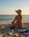 woman sitting crosslegged on the beach on a brightly coloured beach towel looking out to sea