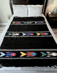 Black blanket with colorful fish patterns on a bed in a bedroom setting.