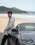 Person standing next to a car on a beach with mountains in the background