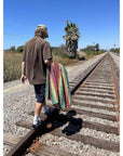 Person walking on train tracks with a colorful striped rasta style Mexican blanket
