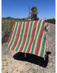Colorful striped blanket on a rocky surface with a clear blue sky.