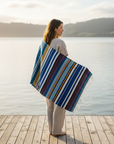 Woman standing on a dock by a lake, wearing a colorful striped blanket.