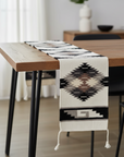 Table runner with geometric pattern on a wooden table in a room with curtains and a vase.