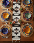 Colorful table setting with patterned plates and placemats on a wooden table.