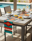 Outdoor dining table set with chairs, colorful table runner, and food by a pool.