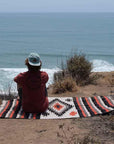 Man sitting on striped and diamond pattern blanket overlooking beach