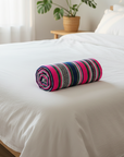 Colorful rolled-up mat on a white bed in a bright bedroom