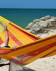 Woman relaxing in a yellow and red hammock by the ocean.