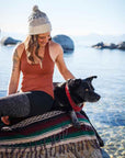 Woman and dog resting on Mexican striped blanket at beach