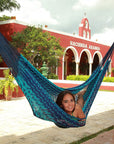 Woman lying in a woven blue hammock in front of a Mexican style hacienda building
