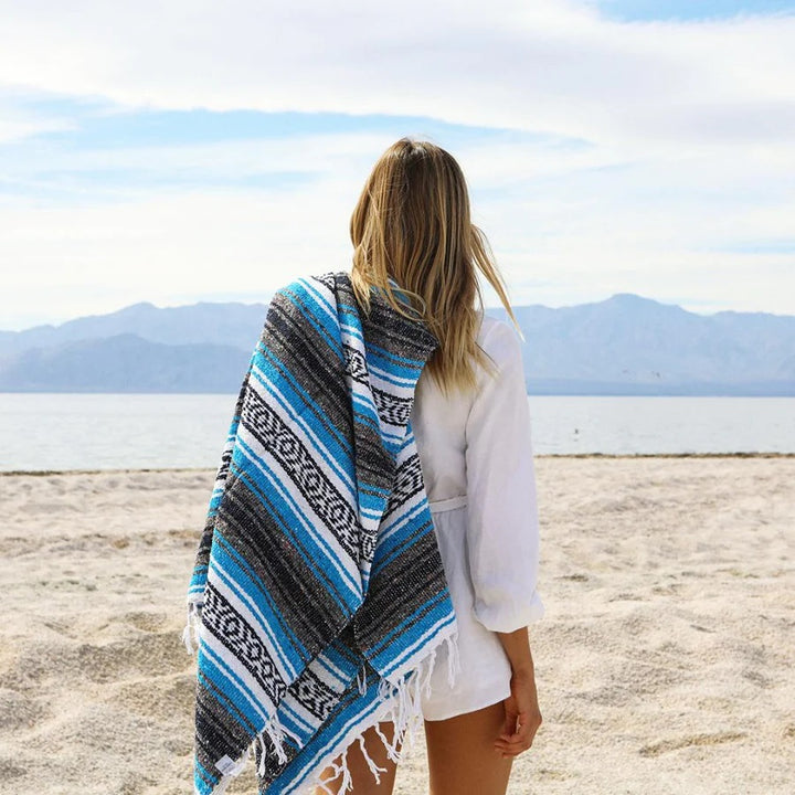 Woman looking out to sea on the beach with a Mexican blanket on her shoulder