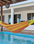 Yellow and red striped hammock hanging by a poolside with a house in the background