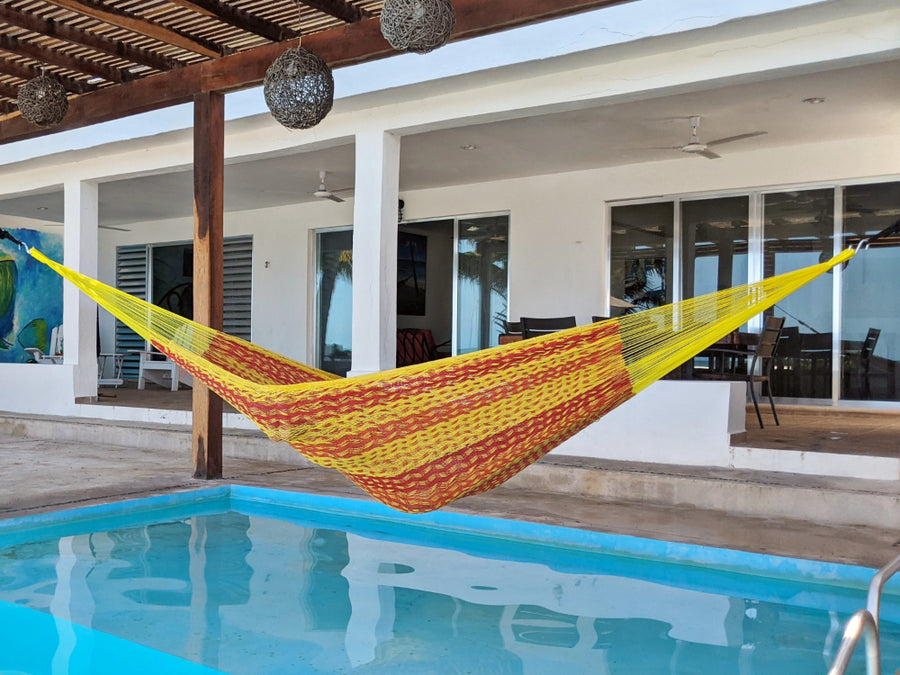 Yellow and red striped hammock hanging by a poolside with a house in the background