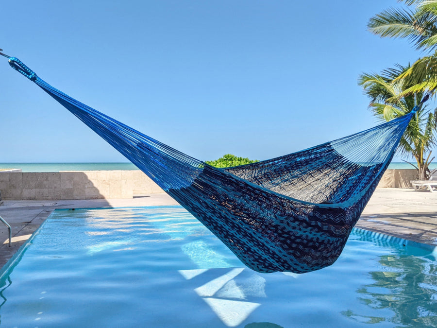 Blue hammock by a pool with palm trees and clear blue sky