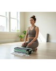 Woman in a yoga pose in a bright room with plants and a yoga mat.