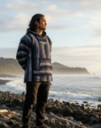 Person wearing a patterned sweater standing on a rocky beach with ocean and cliffs in the background