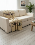 Beige sofa with a patterned throw blanket in a living room setting.