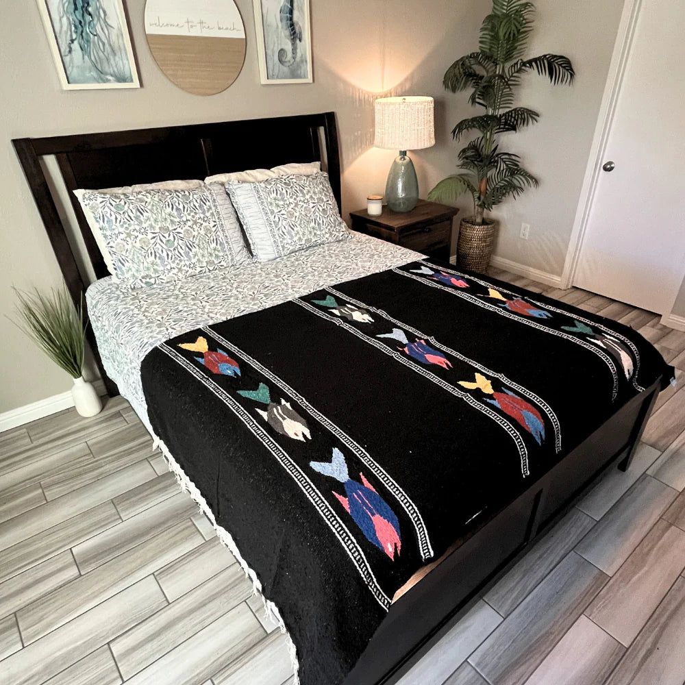 Bed with black and white patterned comforter featuring colorful fish designs in a bedroom setting.