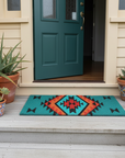 Front porch with a teal door, colorful doormat, and potted plants.