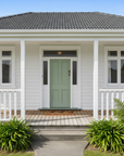 White house with a green door and front porch, surrounded by greenery.