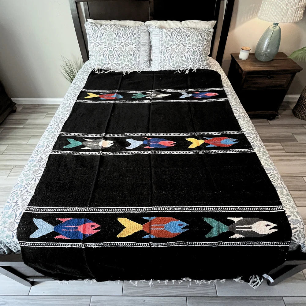 Black blanket with colorful fish patterns on a bed in a bedroom setting.