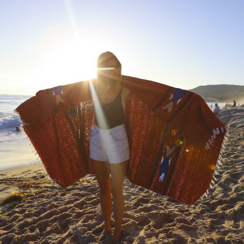 Person holding a large red patterned blanket on a beach