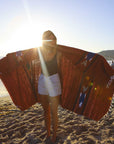Person holding a large red patterned blanket on a beach
