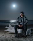Man sitting on a log with a dog on a beach under a full moon