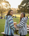 Two people standing at a picnic table in a park with trees and grass in the background.
