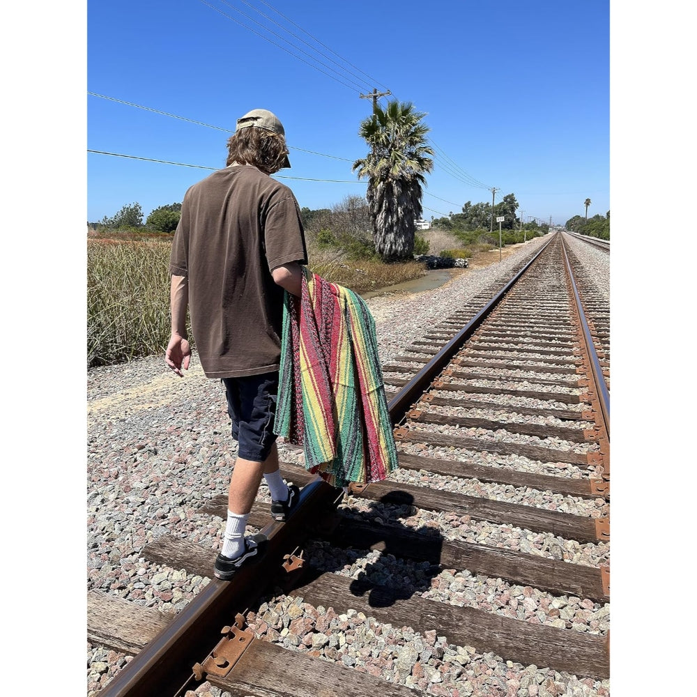 Person walking on train tracks with a colorful striped rasta style Mexican blanket
