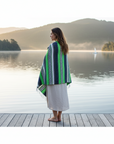 Woman standing on a dock by a lake, wearing a colorful striped shawl.