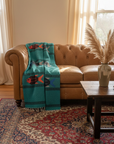 Teal Fish Blanket in living room on leather couch with patterned rug