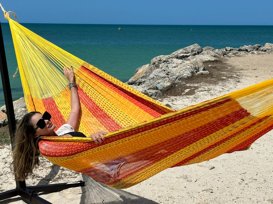 Woman relaxing in a yellow and red hammock by the ocean.