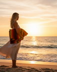 Woman holding a colorful towel on a beach at sunset