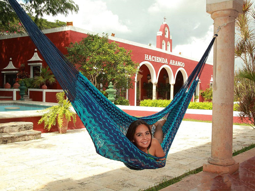 Woman lying in a woven blue hammock in front of a Mexican style hacienda building